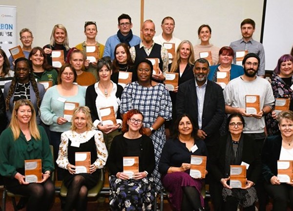 A group of people holding an orange brochure smiling to the camera