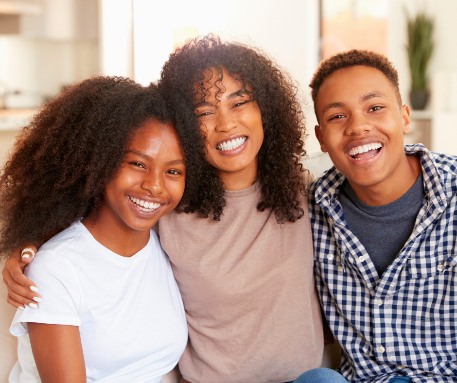 A mother between her son and daughter, smiling with their arms around each other.