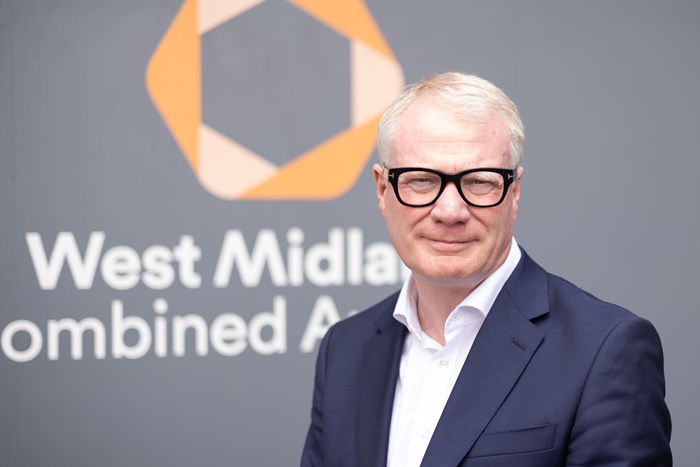 Portrait photo of the Mayor in front of a West Midlands Combined Authority sign