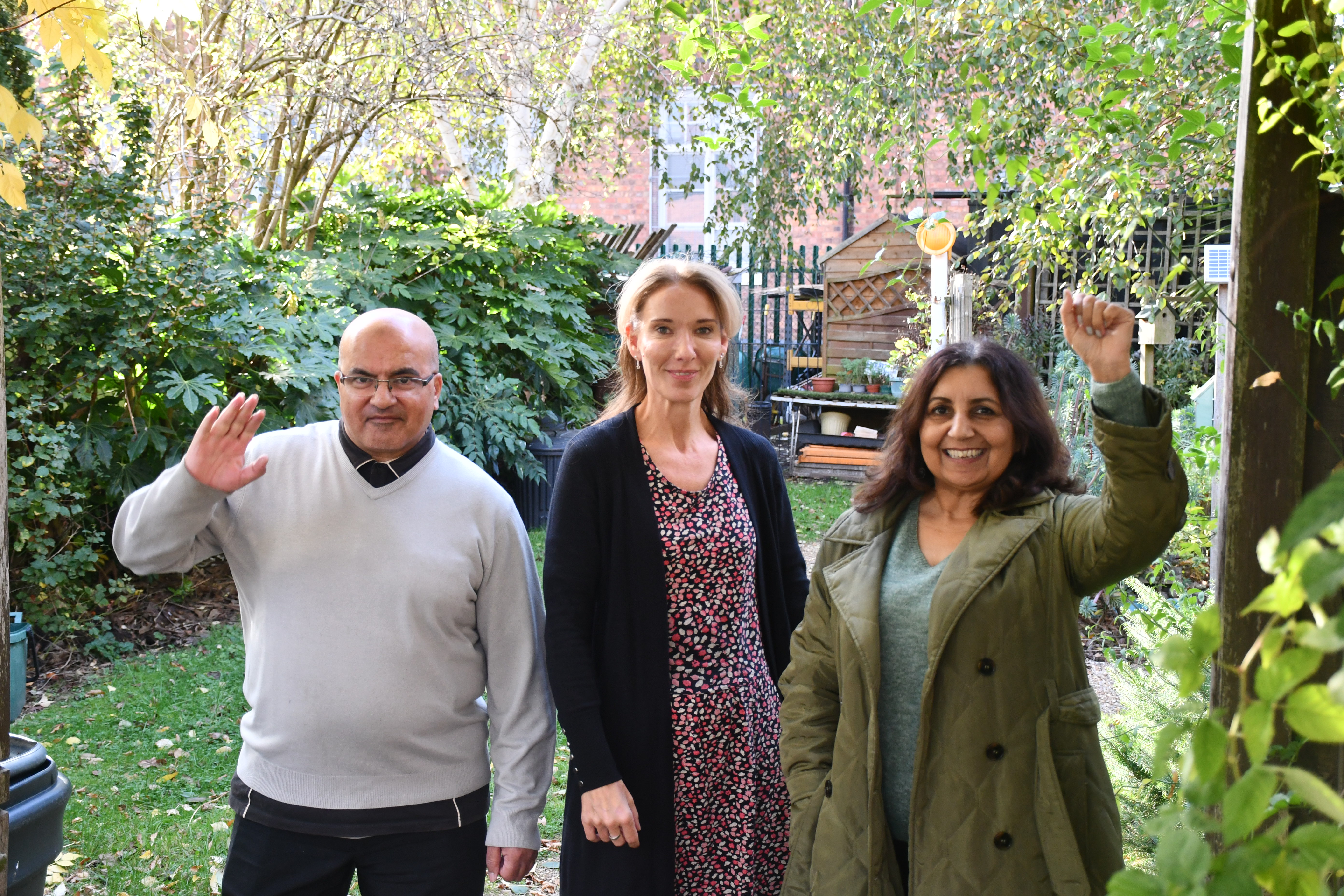 Three people, a man, and two women, standing in a garden under and archway