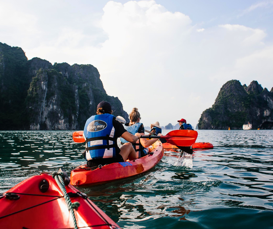 A group of people in orange kayaks on the water, with tall rocks in the distance.