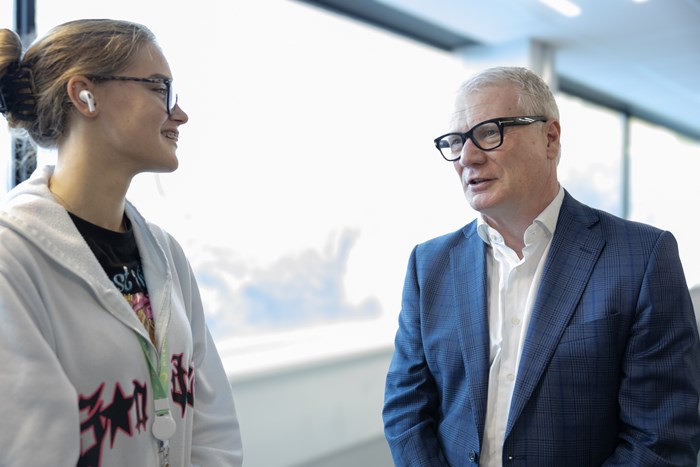 Two people having a conversation in a modern educational setting, standing near large windows and natural light.