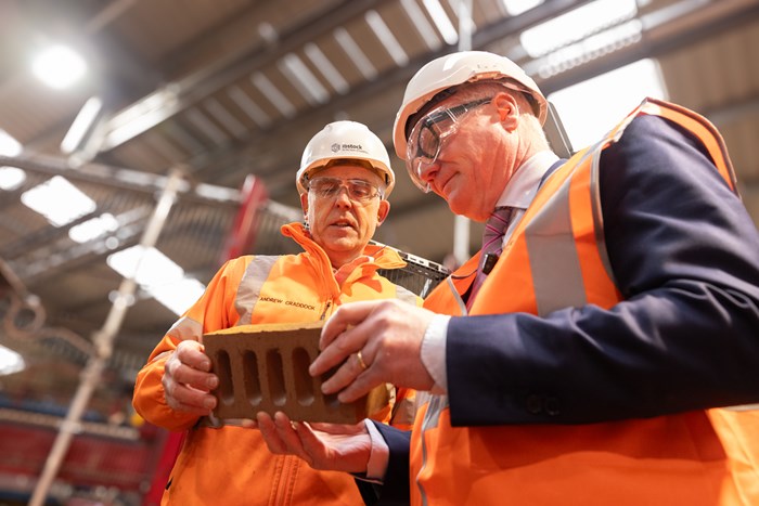 Two men wearing hi-vis jackets holding a brick together