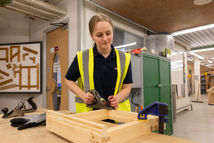 A female sanding a piece of wood inside a workshop.