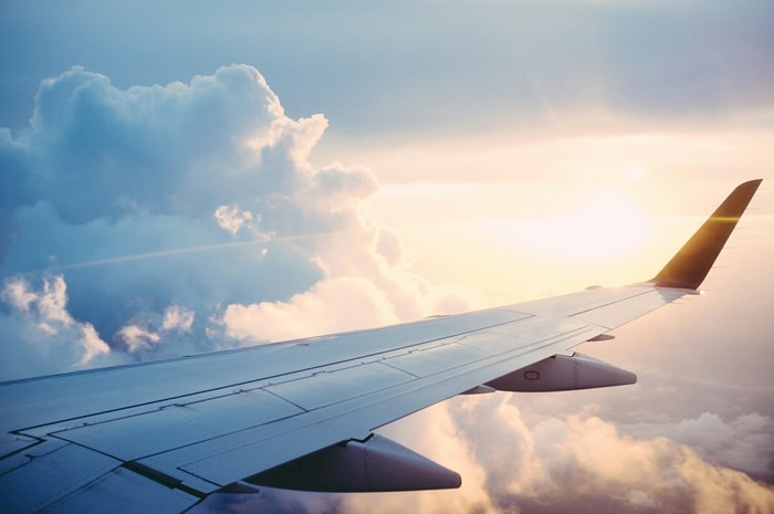 The wing of a plane in the sky with clouds and the sun setting in the background