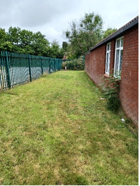 Gassed land outside a building to the right with a metal fence bordering the grass to the left