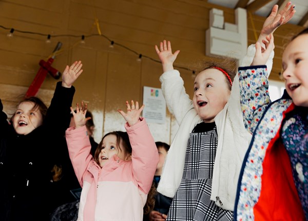 An photograph of four young children having fun with their arms outstretched in the air.