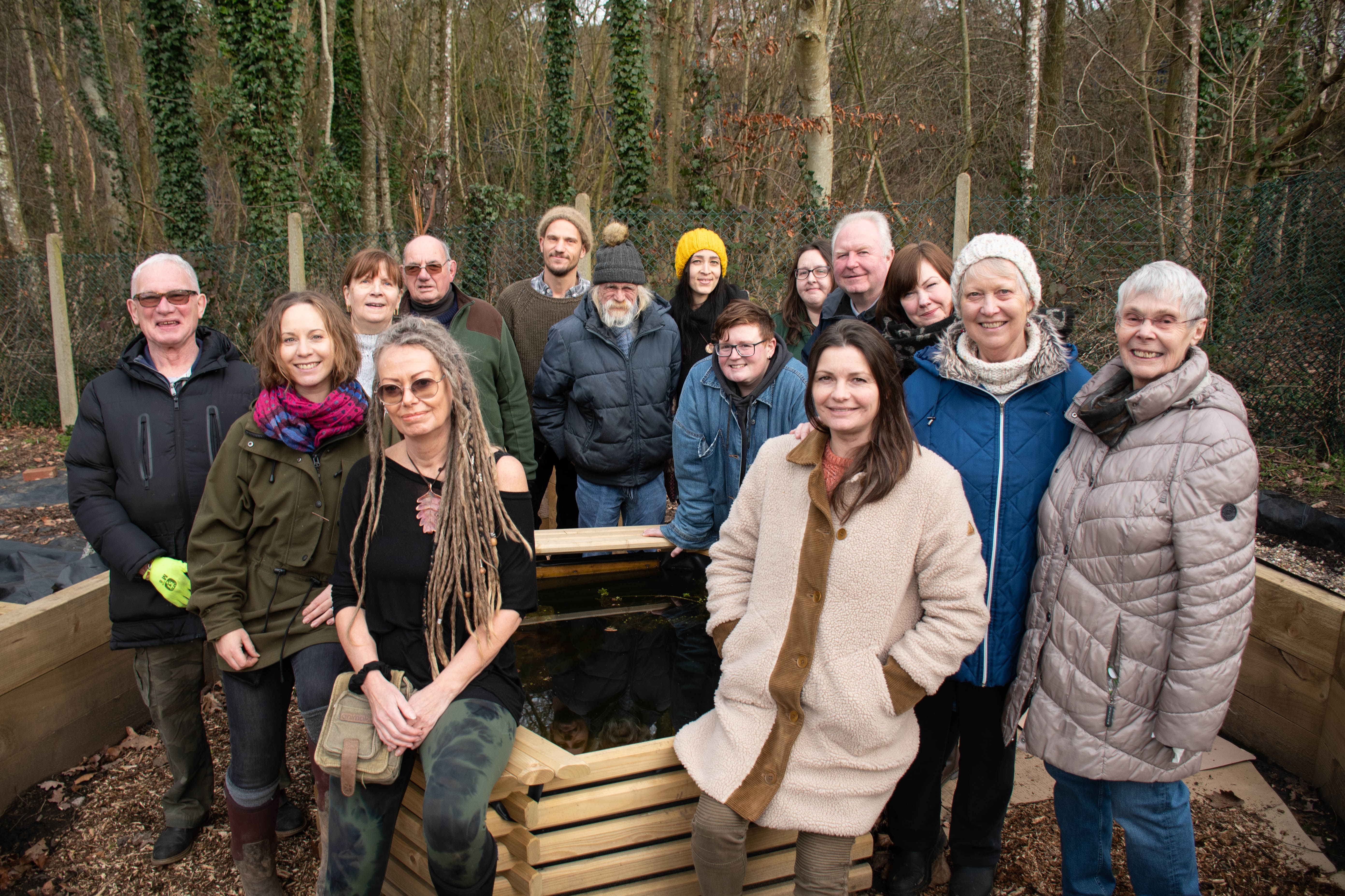 A community group standing in front of a woodland area smiling to the camera
