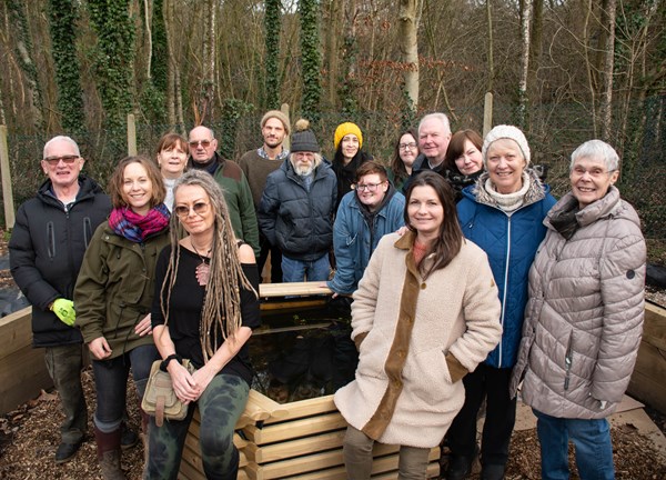 A community group standing in front of a woodland area smiling to the camera