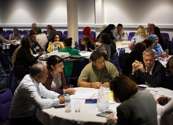 Groups of people seated at round tables in a conference room working together in discussion