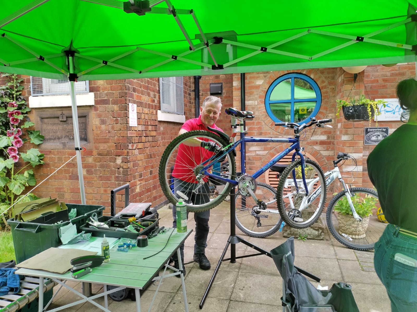  A person fixing a bike stood under a green gazebo