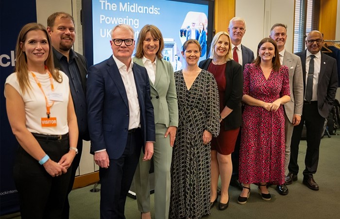Group of professionals posing for a photo at an event, with a presentation screen in the background displaying 'The Midlands: Powering UK'.