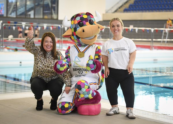 A woman poses with Perry the Bull (official mascot of Birmingham Commonwealth Games 2022) and Paralympian Swimmer, Ellie Simmonds at the side of a swimming pool.