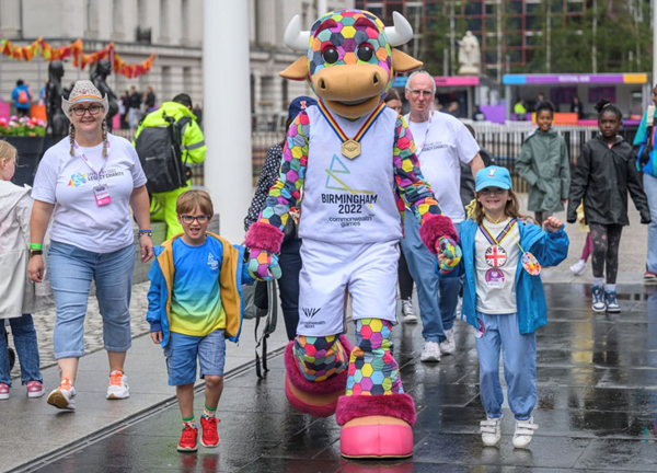 People walking hand in hand wearing Birmingham 2022 merchandise alongside Games' mascot Perry the Bull 
