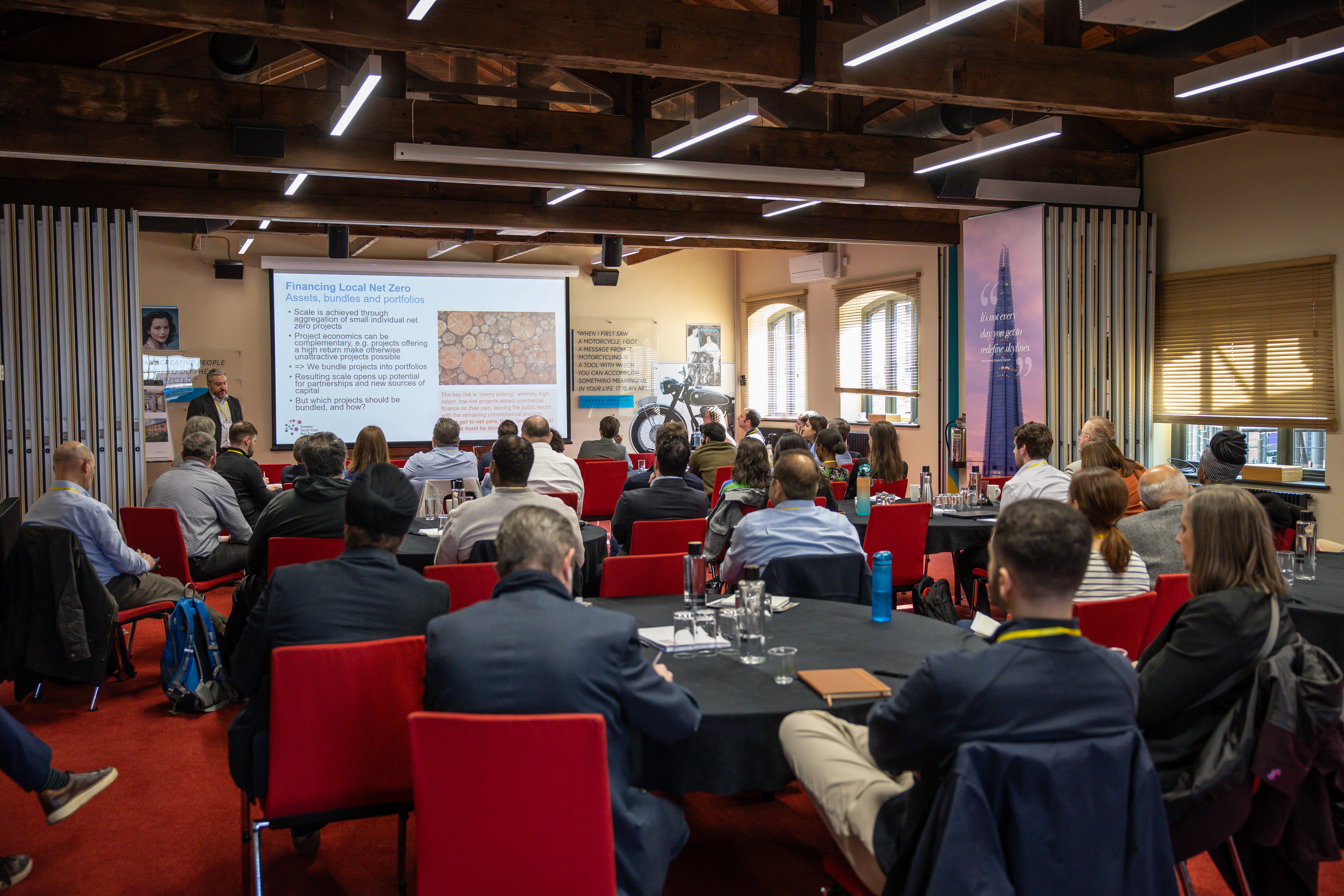 A photo of a conference room with guests and powerpoint display in the background