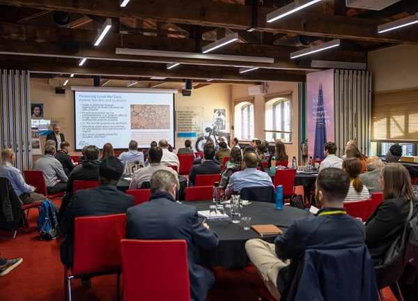 A photo of a conference room with guests and powerpoint display in the background
