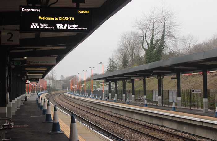 Shows platforms either side of a railway track heading off into distance. A sign under the platform canopy says Welcome to Kings Heath