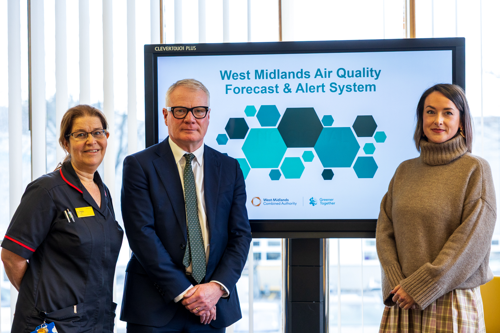 Three people stand before a screen displaying "West Midlands Air Quality Forecast & Alert System." They appear professional and engaged.
