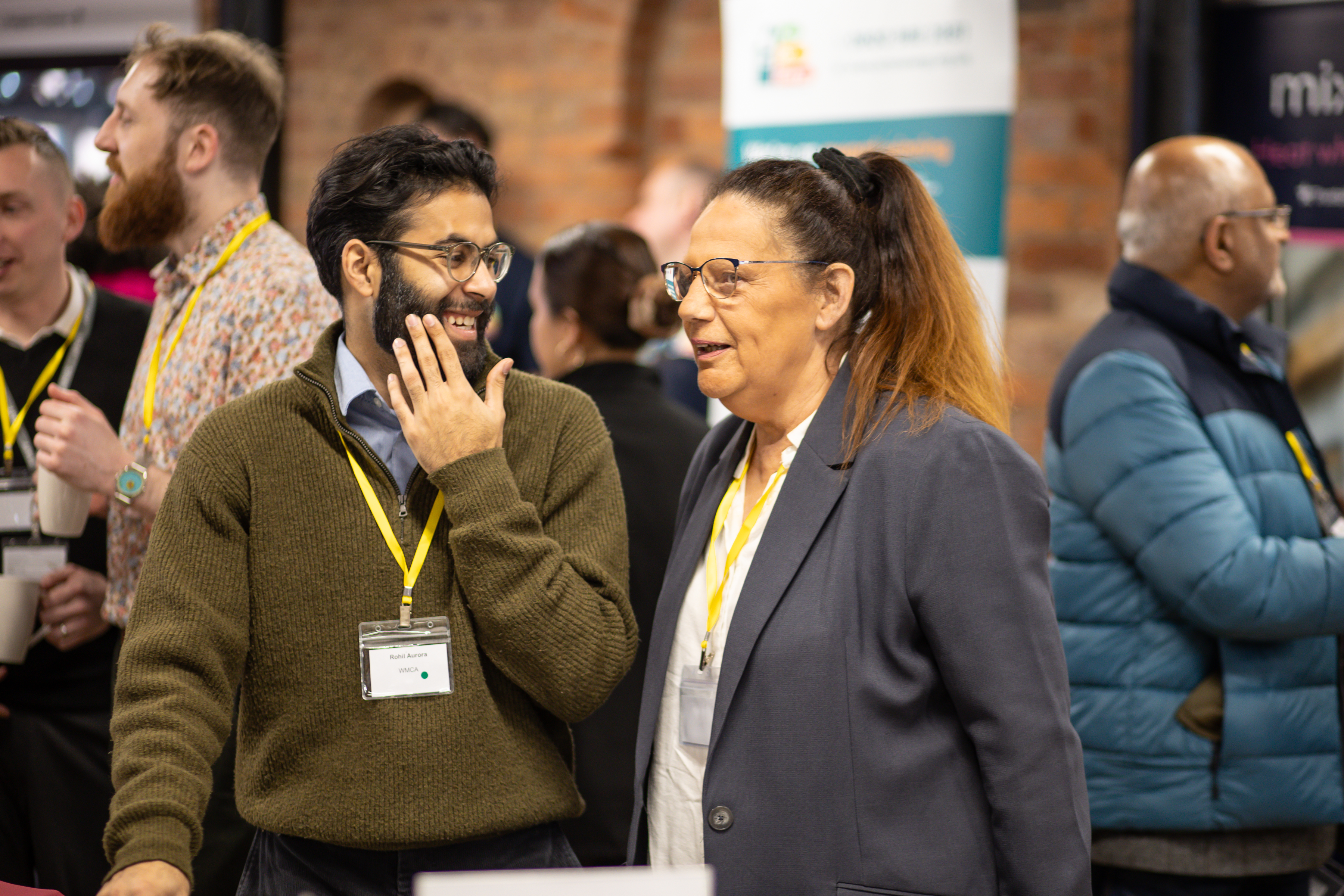 Two guests at the event, one man and woman wearing lanyards talking to eachother.
