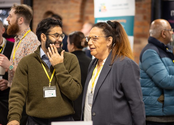 Two guests at the event, one man and woman wearing lanyards talking to eachother.