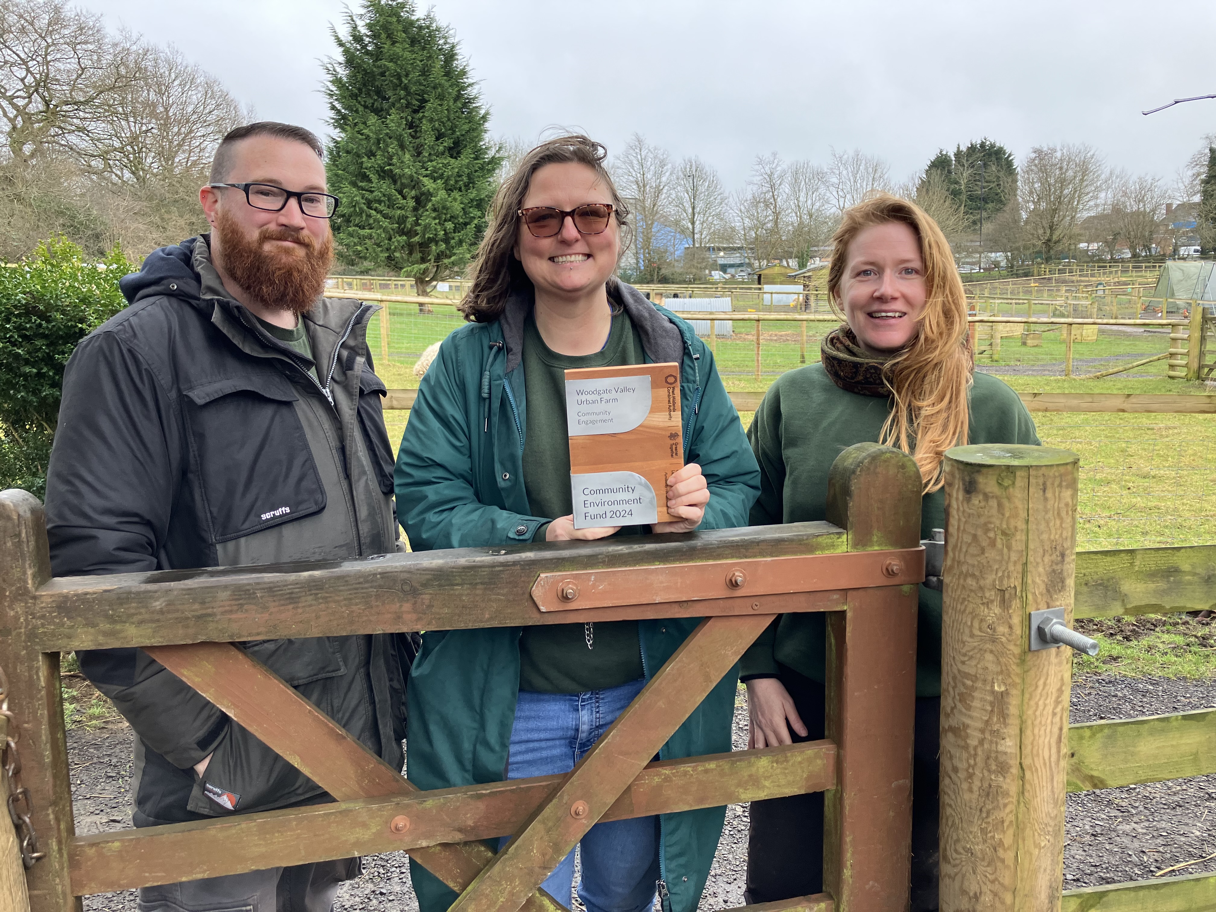3 people at a farm holding a brochure and smiling to the camera